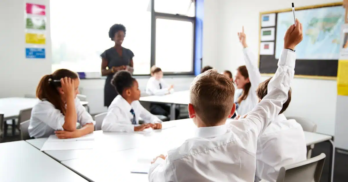Schoolchildren with hands raised in classroom