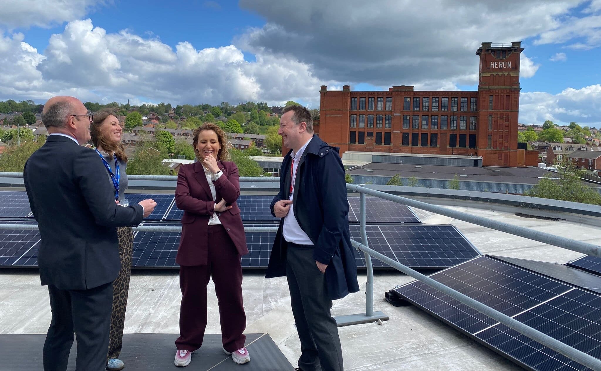 Four men and women in business attire on a roof surrounded by solar panels